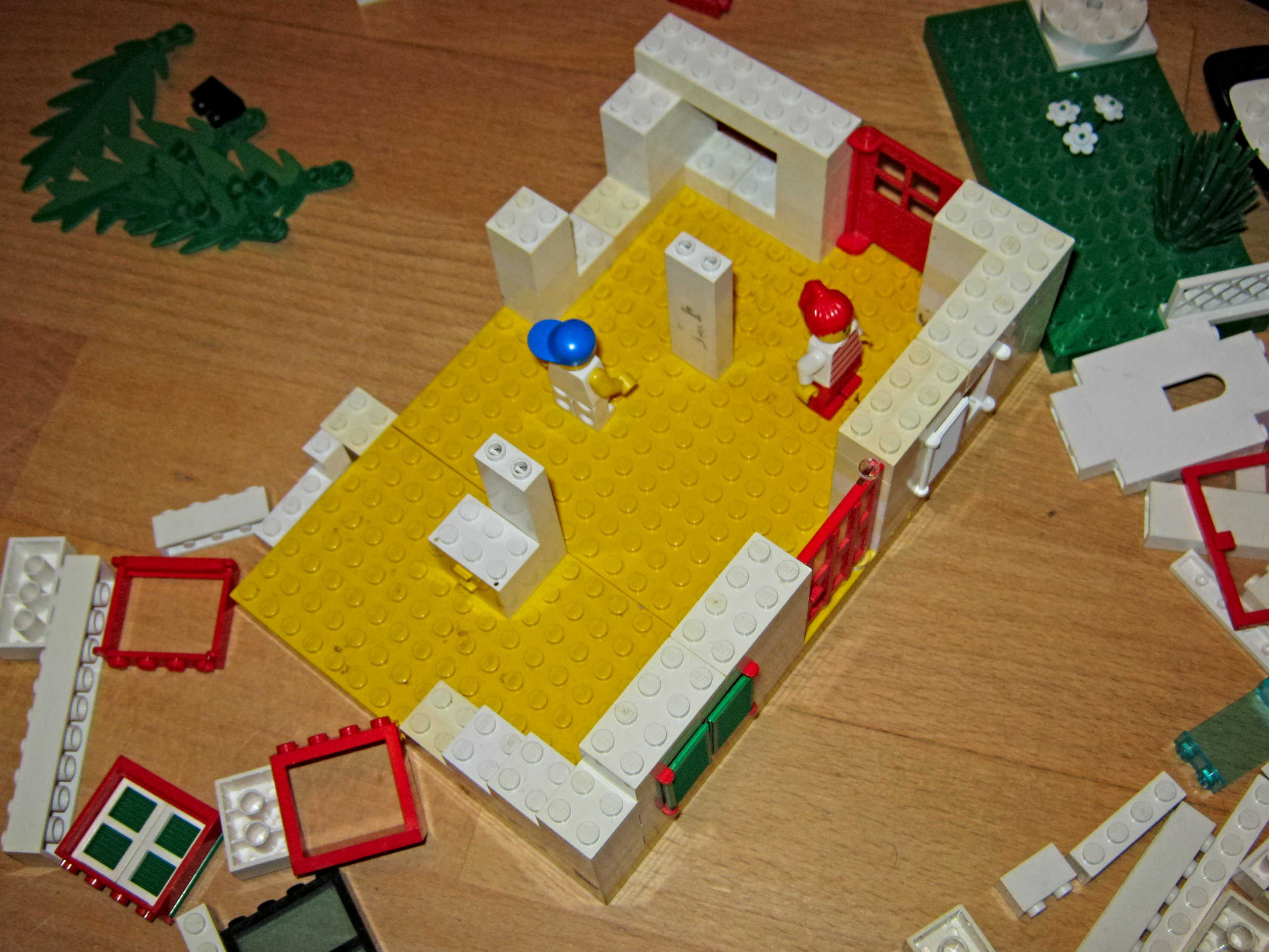 A house made of toy bricks in its early stages; there is just the baseplate and some provisional walls.
